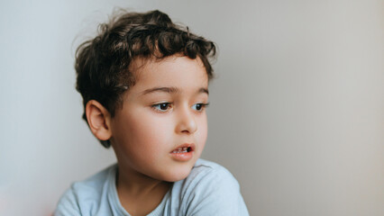Handsome caucasian curly baby boy sitting at home wants to play outside. Cute curly hispanic kid dreaming with pensive face, feels offence. Little Caucasian child sad, frustrated. Childhood.
