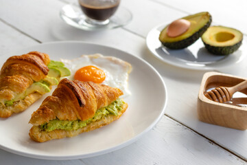 Croissant sandwich with egg,avocado on white dish and honey, coffee. breakfast and healthy food concept.