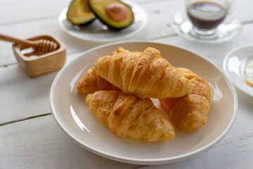 Croissant with egg,avocado on white dish and honey, coffee. breakfast and healthy food concept.