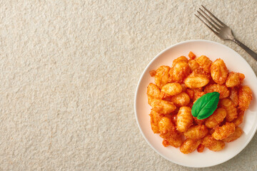 White plate of freshly prepared POTATO GNOCCHI in tomato sauce and basil. Marble stone background. Top view from copy space.