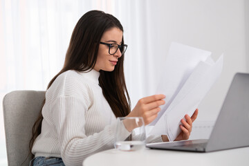 Smiling young businesswoman in glasses looking at the documents and check with notebook. 