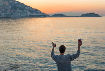 back happy woman celebrating with raised arms looking at the sunset in front of the sea. Enjoying live in a beatiful lanscape. Concept of happiness, joyful people. 