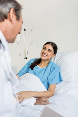 Obraz premium Smiling patient in gown talking to blurred doctor in hospital.