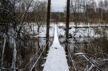Suspension wooden bridge covered in snow on a winter morning after a snowfall.