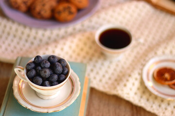 Plate of cookies, cup of tea, fresh blueberries, dry oranges, stack of books, reading glasses and tablet on the table. Hygge at home. Selective focus.