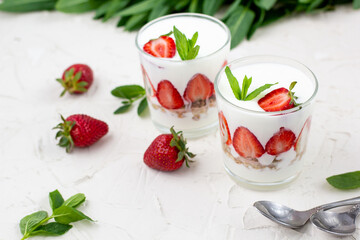 White yogurt with fresh strawberries granola and mint in two glasses on a white background.