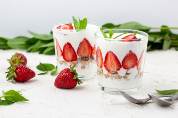 White yogurt with fresh strawberries granola and mint in two glasses on a white background.
