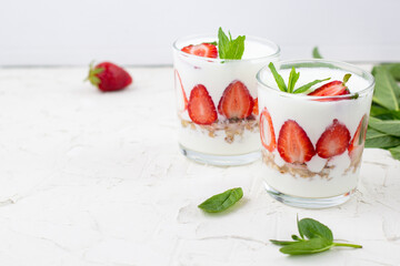 White yogurt with fresh strawberries granola and mint in two glasses on a white background.