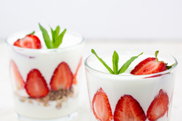White yogurt with fresh strawberries granola and mint in two glasses on a white background.