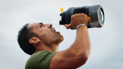 Athlete quenches his thirst with bottles of water - obrazy, fototapety, plakaty