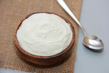 White fermented milk yogurt in a decorative plate, next to a metal spoon, on a brown background
