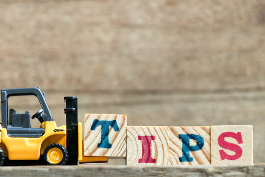 Toy yellow forklift hold letter block t to complete word tips on wood background