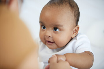 African baby girl learning to walk and mother or sitter holding hands on bedroom