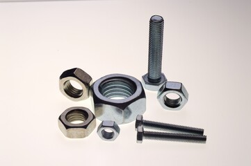 New, chrome-plated bolts and nuts of different sizes lie on a white background. Close-up