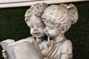 girls reading, plaster figure Old white statue of children reading a book.