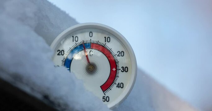 Thermometer with celsius scale in snow demonstrates ambient temperature rising up from minus 6 degrees to zero - spring weather change or global warming concept 4K timelapse