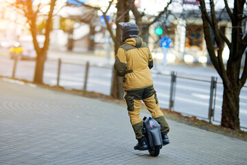 Man riding fast on unicycle through city street. Stylish man in safety gear and protective helmet riding electric self balancing monowheel outdoor. Convenient self mobility transport © Tricky Shark