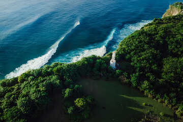 Aerial view of coastline with lighthouse and ocean with ideal blue waves in Uluwatu, Bali