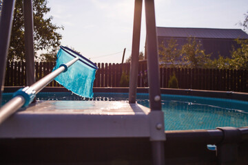 Abstract blur and defocused background. Cleaning of a swimming pool with a metal frame with a mesh from dirt. Pool cleaner during operation. Solar banner.The concept of summer holidays.