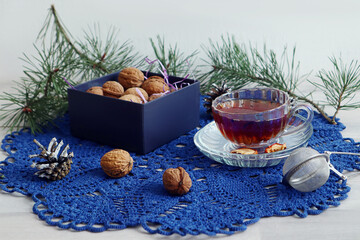 Winter still life: a cup of tea with walnuts in a box on a blue lace napkin against a background of pine branches