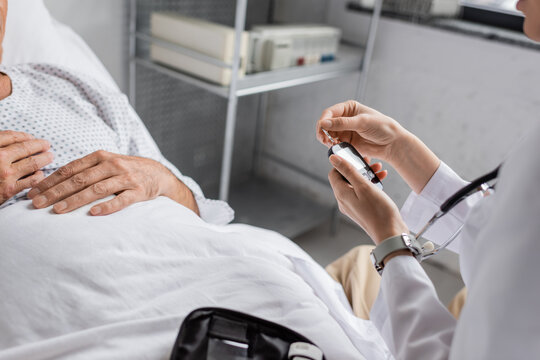 Cropped view of doctor holding glucometer near elderly patient in clinic.