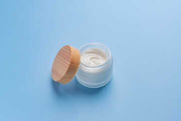 face cream on blue background. Professional frosted glass jar with bamboo lid for facial and body...
