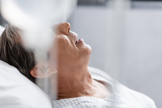 Sick elderly patient lying near blurred intravenous therapy in hospital.
