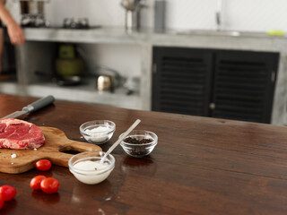 Stylish kitchen, on a wooden table there is a piece of fresh meat with spices, tomatoes and herbs, minimalist interior
