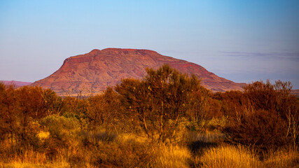 Fototapeta premium Sunrise over mighty mountains in karijini national park in western australia; Australian outback with red rocks, distinctive trees and mountains in the background