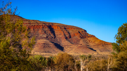 Sunrise over mighty mountains in karijini national park in western australia; Australian outback with red rocks, distinctive trees and mountains in the background