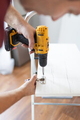 Close up man holding cordless screwdriver machine and screws lie for screwing a screw assembling furniture at home - obrazy, fototapety, plakaty