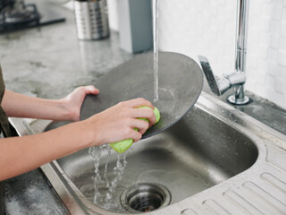 Woman with hands without gloves washes dishes with a dishwashing sponge with bubbles close-up, household chores, no dishwasher, high water consumption. Stylish kitchen design, house cleaning