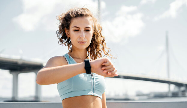 Portrait of a sporty strong woman checks progress on a smartwatch. A female runner looks at a smart watch with a heart rate monitor and a heart rate monitor.