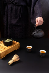 Женщина в черном кимоно проводит чайную церемонию