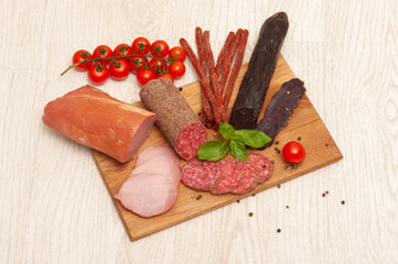 Different types of sausages ham, mahan, salami on a wooden board decorated with tomatoes and basil