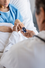 Fototapeta na wymiar Blurred doctor wearing pulse oximeter on finger of patient in hospital.