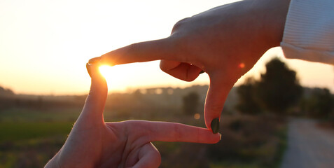 woman's hand creates a frame in front of the sun. idea of vision and focus - obrazy, fototapety, plakaty