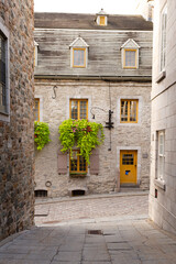 Fototapeta na wymiar Selective focus view of beautiful stone historic 17th century house seen at the end of a narrow old town street, Petit-Champlain sector, Quebec City, Quebec, Canada