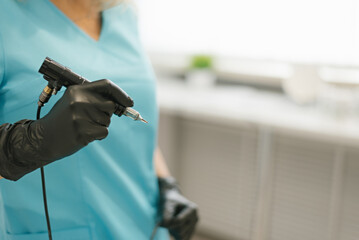 Master of permanent makeup in blue medical suit with tool in hand. Closeup