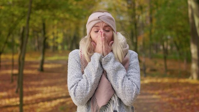 Front view of shocked, frightened woman standing in park, looking at camera. Beautiful, blonde female wearing stylish clothes, closing eyes, showing no. Concept of autumn and fall.