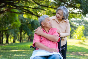 Senior couple in the park and wife taking care of a husband in a wheelchair a patient with paralysis, with his wife comforting and encouraging each other. Retirement health insurance concept.