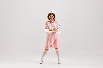 Emotional young woman, retro waitress in american fashion style of 70s, 80s uniform posing over light studio background. Comic photography style