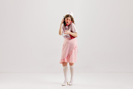 Emotional young woman, retro waitress in american fashion style of 70s, 80s uniform posing over light studio background. Comic photography style
