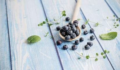 Fresh juicy blueberries with green leaves on a blue background. Healthy berry, organic food, vitamin, blue food.