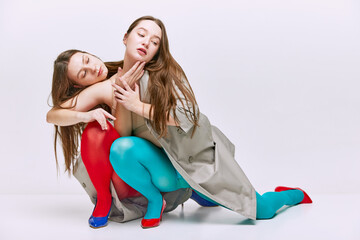 Beauty. Portrait of two young girls in bright red and blue tights and coat posing over grey studio...