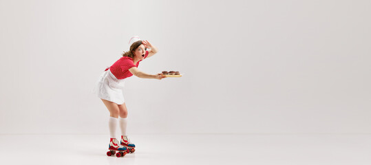 Pin Up style portrait of beautiful young girl in image of retro cater waiter wearing 70s, 80s fashion style uniform and rollers isolated over light studio background.