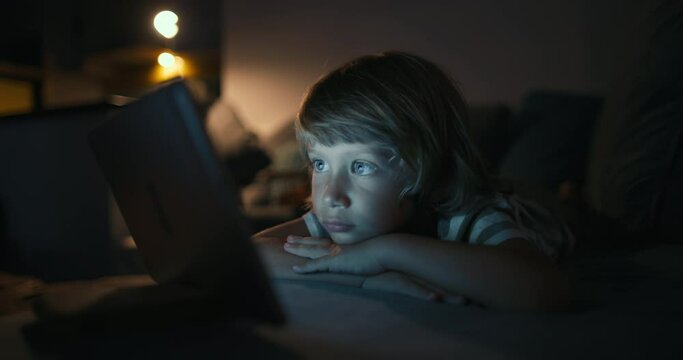Close up of boy 4-5 years child while using a tablet Concept, kid dream online video games at night concept. caucasian boy watching online video, digital tablet network. child on social media