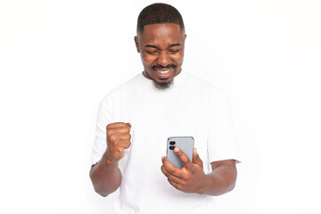 Satisfied young man looking at smartphone screen. Male African American model with brown eyes, short haircut and beard in white T-shirt using smartphone with face of winner. Success concept