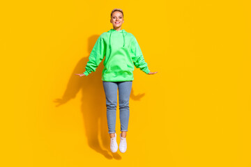 Full length photo of young active lady jump up trampoline demonstrate satisfied her sporty casual clothes promo isolated on yellow color background