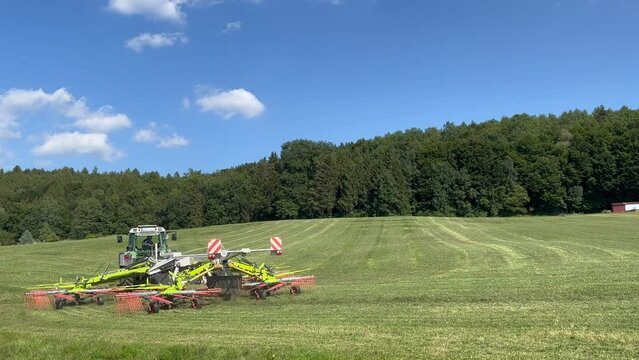 Tractor raking grass crop into rows for baling
